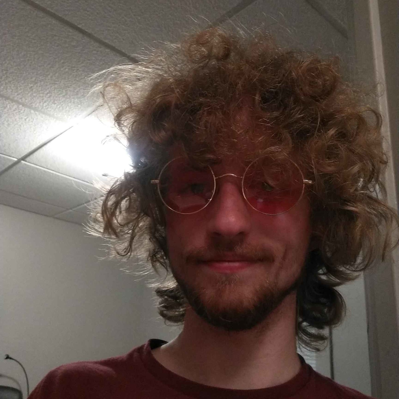 A picture of Calvin wearing a red t-shirt and red-tinted glasses. They are smiling at the camera.