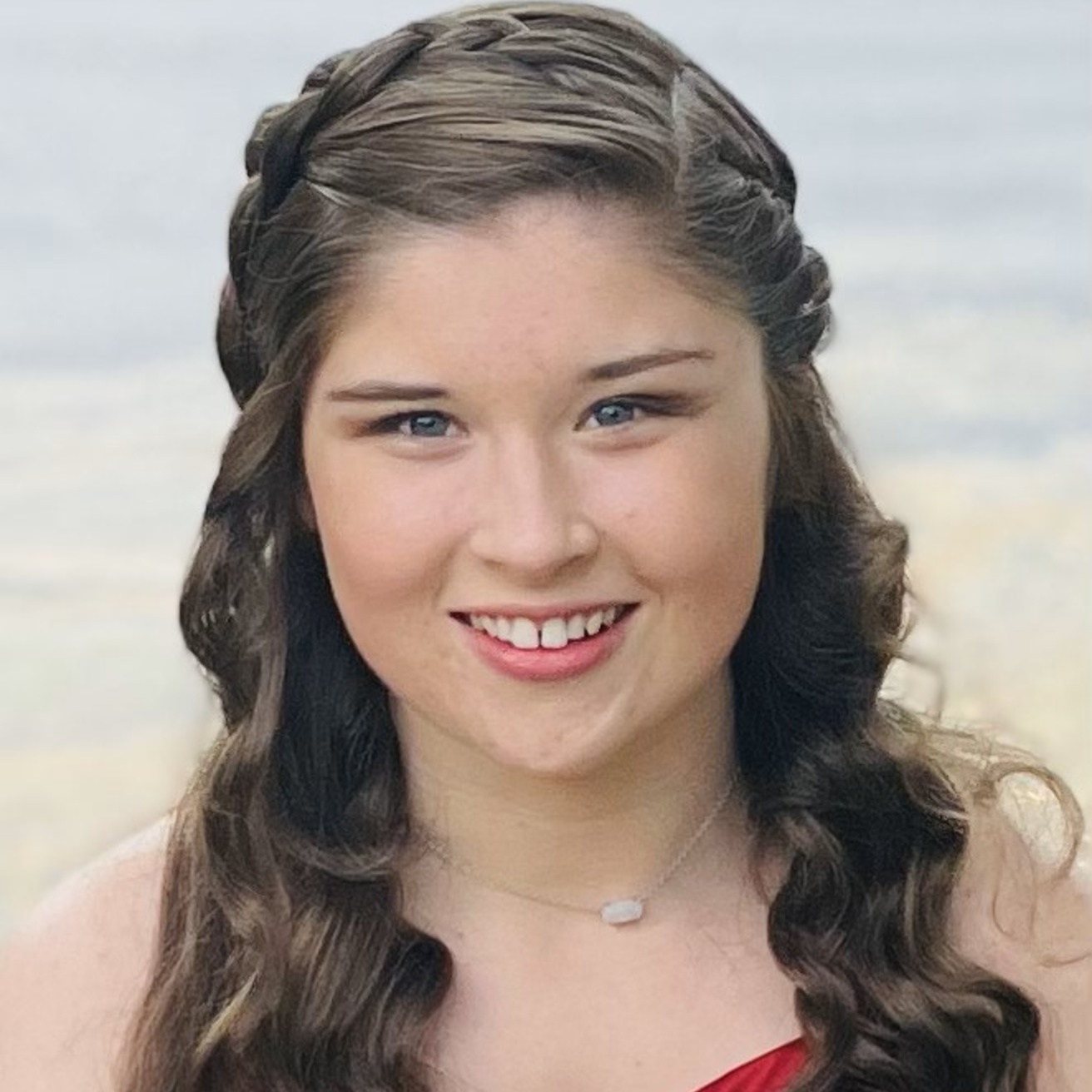 A picture of Morgan in a scoop-neck red dress. Her hair is half-up, half-down, and falls in curls over her shoulders. Her bangs are pinned back and she is smiling brightly.